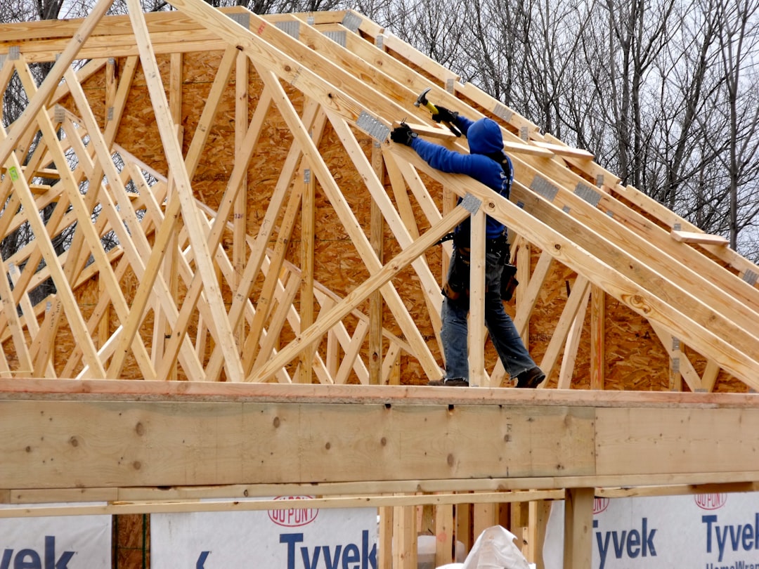 Framing crew setting roof trusses on a new home, showing crane or telehandler placement and temporary bracing